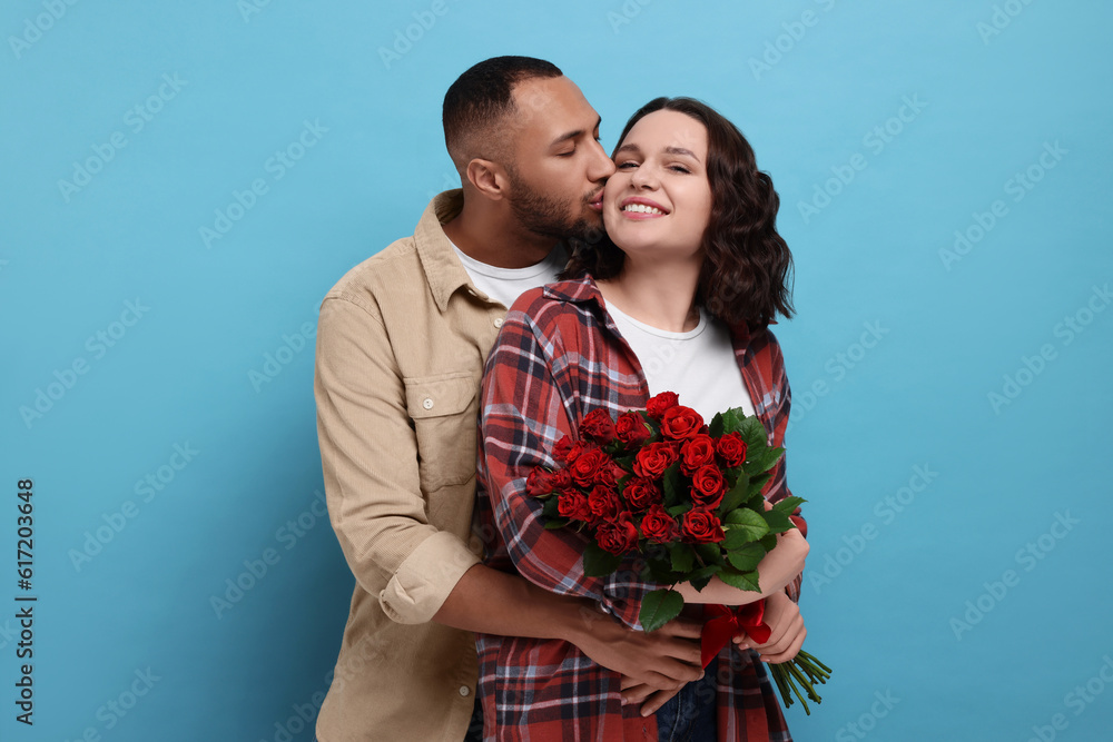 Happy couple celebrating Valentine's day. Beloved woman with bouquet of red roses on light blue background Happy couple celebrating Valentine's day. Beloved woman with bouquet of red roses on light blue background