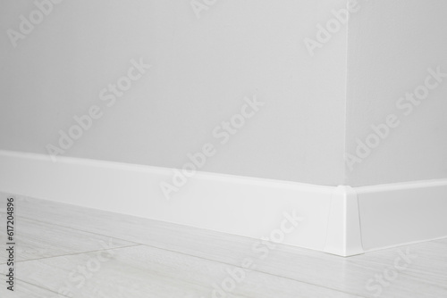 White plinth with connector on laminated floor near wall indoors, closeup