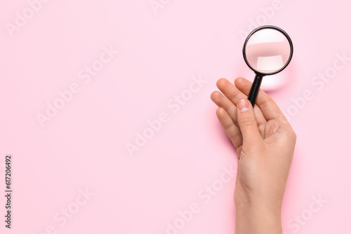 Female hand with magnifier on pink background photo