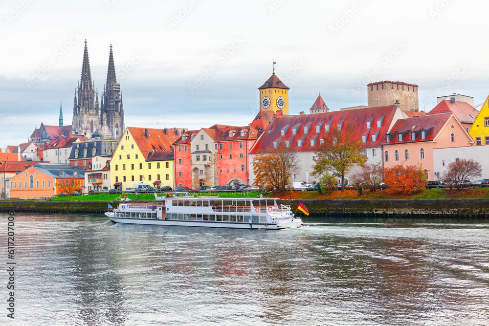 Regensburg city on a river in Bavaria , Germany . Tourist boat on the Danube river in Regensburg . Clock tower and cathedral at riverside in autumn 