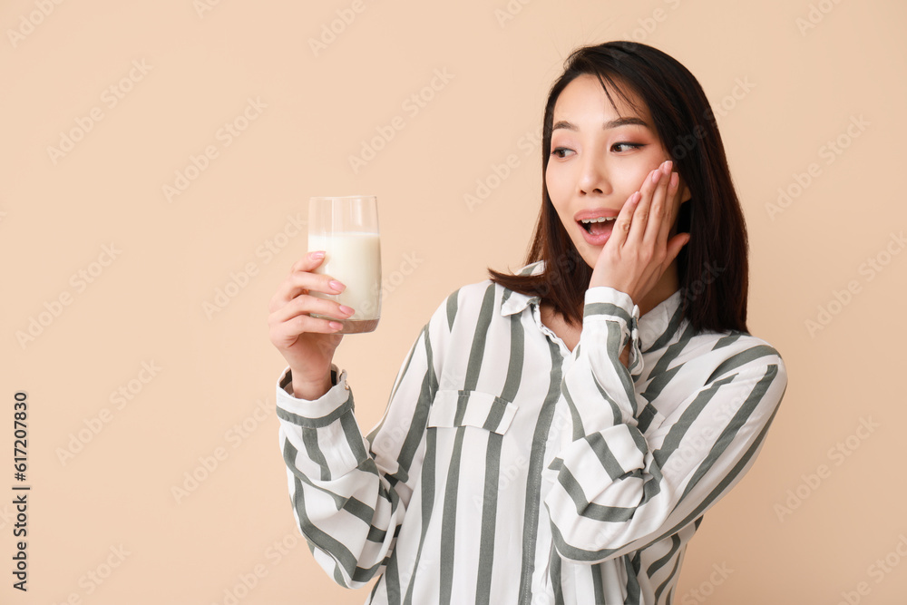 Surprised Asian woman with glass of milk on beige background Surprised Asian woman with glass of milk on beige background