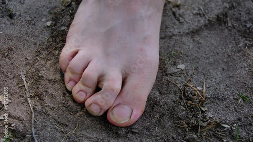 Close up of barefoot toes with slightly dirty nails while standing on sandy ground.