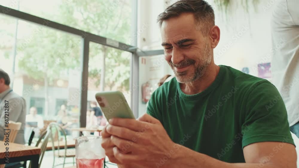 Middle-aged man sitting in cafe watching videos on mobile phone Middle-aged man sitting in cafe watching videos on mobile phone