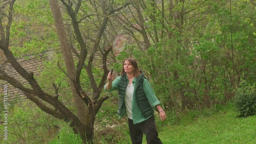 Woman relaxing in nature, playing badminton in a home garden. Female leisure activity outdoors. Child free weekend. Woman relaxing in nature, playing badminton in a home garden. Female leisure activity outdoors. Child free weekend.