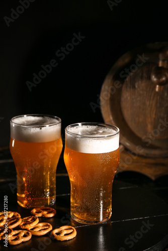 Glasses of cold beer with pretzels on dark background