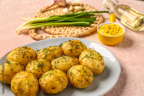 Plate of boiled baby potatoes with dill and green onion on pink background