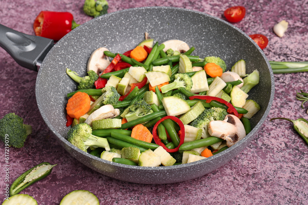 Frying pan with fresh vegetables on purple background Frying pan with fresh vegetables on purple background