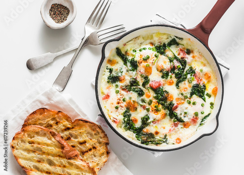 Baked shakshuka with spinach, tomatoes and mozzarella in a cast-iron pan and grilled ciabatta on a light background, top view