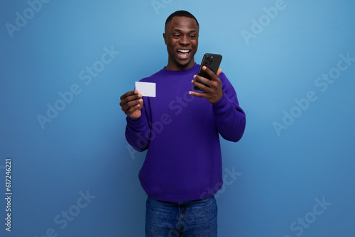 handsome young american man in blue sweatshirt pays the bill online with card and smart phone