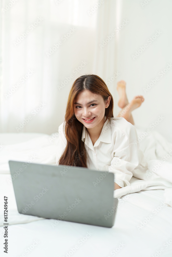 Happy smiling asian woman stretching on bed in the morning and using laptop computer Happy smiling asian woman stretching on bed in the morning and using laptop computer