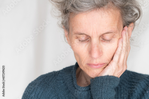 Close up head and shoulders view of older woman in blue sweater with eyes closed and hand on head (selective focus)