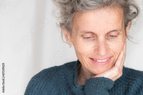 Close up head and shoulders view of older woman in blue sweater smiling with head in hand (selective focus)