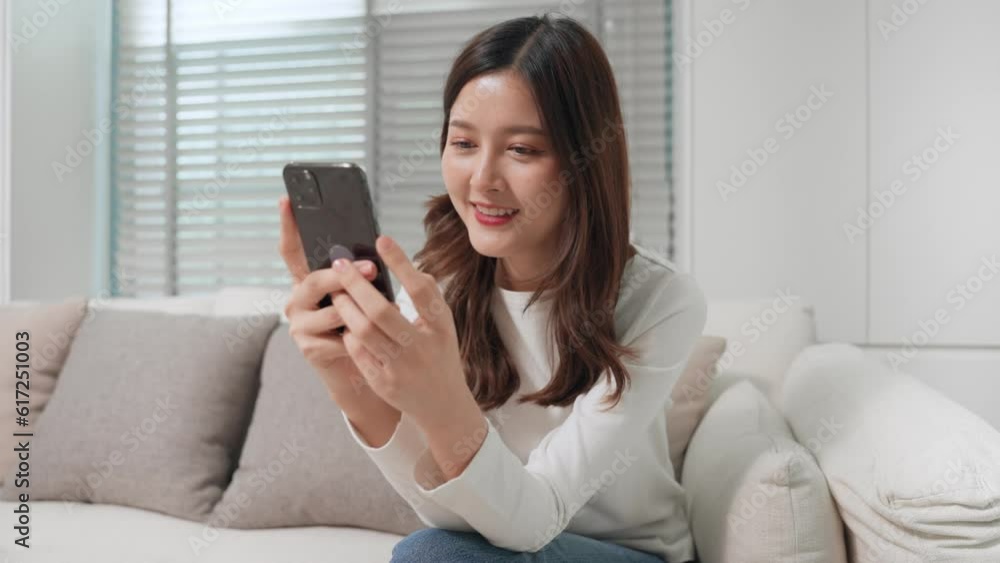 Happy Asian teen girl holding and using mobile phone in living room at home. Smiling Asia woman typing smartphone chat with friend feel happy and relaxed on holiday. Lifestyle and technology concept Happy Asian teen girl holding and using mobile phone in living room at home. Smiling Asia woman typing smartphone chat with friend feel happy and relaxed on holiday. Lifestyle and technology concept