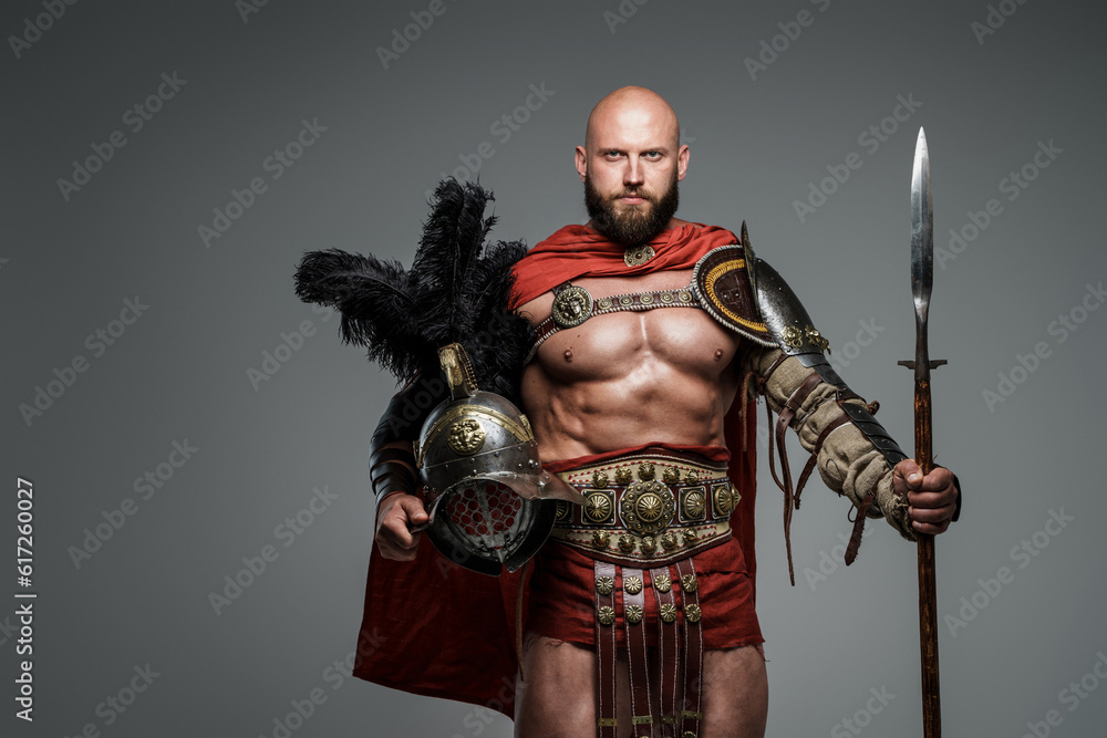 Confident bald gladiator with light armor and red cape, holding a spear and gladiator helmet with feathers, staring down the camera on a neutral gray background Confident bald gladiator with light armor and red cape, holding a spear and gladiator helmet with feathers, staring down the camera on a neutral gray background