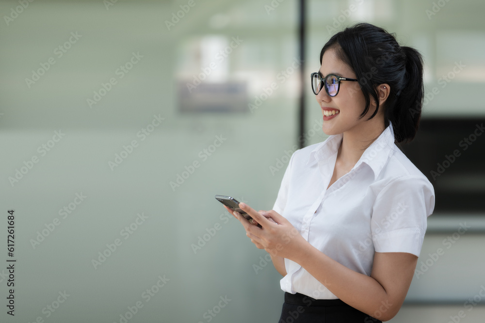 Portrait of an Asian smiling businesswoman standing holding and using a smartphone. Portrait of an Asian smiling businesswoman standing holding and using a smartphone.