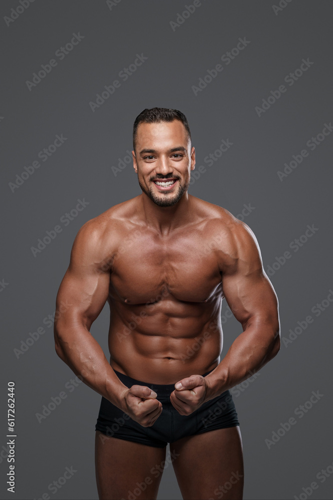 Breathtakingly handsome male model with a chiseled physique flashes a charming smile as he poses in black briefs against grey background, emanating charisma and sex appeal Breathtakingly handsome male model with a chiseled physique flashes a charming smile as he poses in black briefs against grey background, emanating charisma and sex appeal