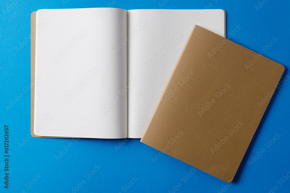 Close up of beige notebook and open book with copy space on blue background Close up of beige notebook and open book with copy space on blue background