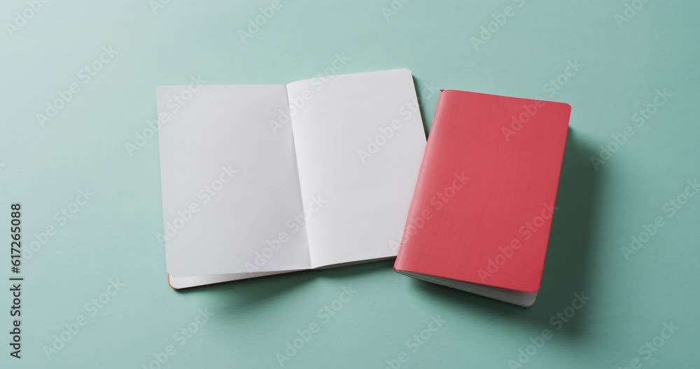 Close up of open blank book and closed red book with copy space on green background in slow motion Close up of open blank book and closed red book with copy space on green background in slow motion