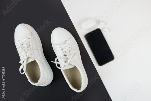 Top view photo of white sneakers with phone and headphones on black and white background