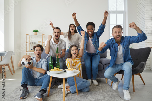 Quadro em tela Multinational group of friends of fans gathered in front of the TV to watch a football match together, sitting on the sofa in room at a coffee table