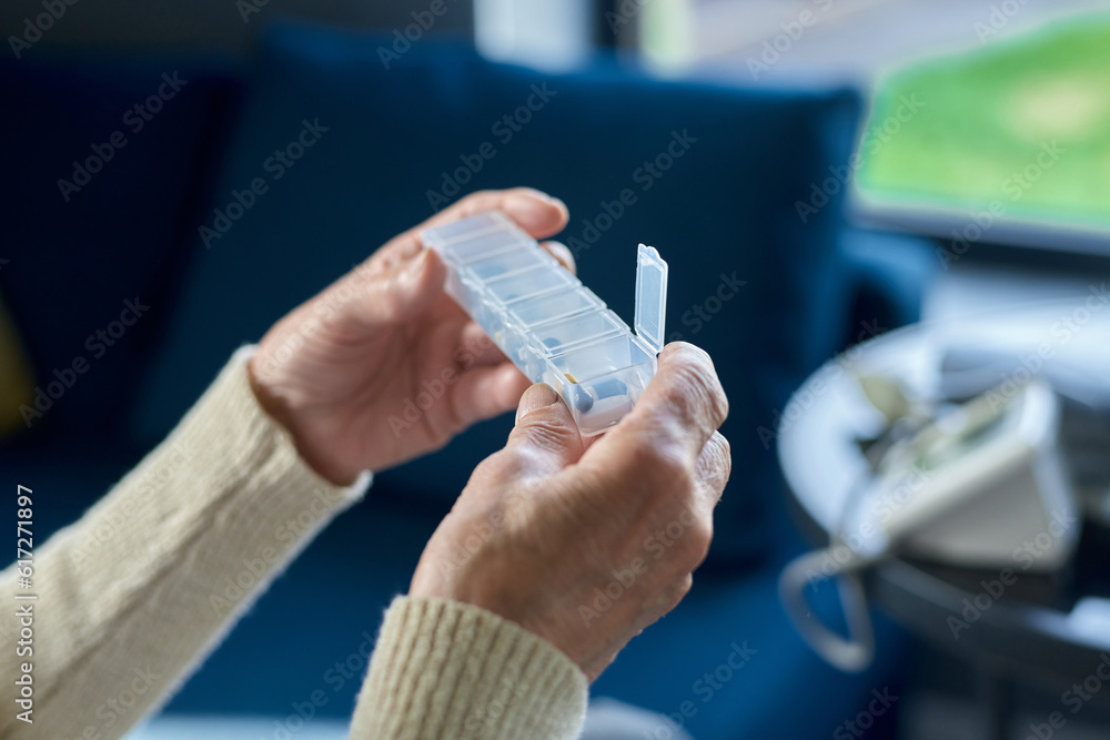 Close-up of hands of sick senior woman holding small plastic pill-box or container with pills for therapy course while going to take one