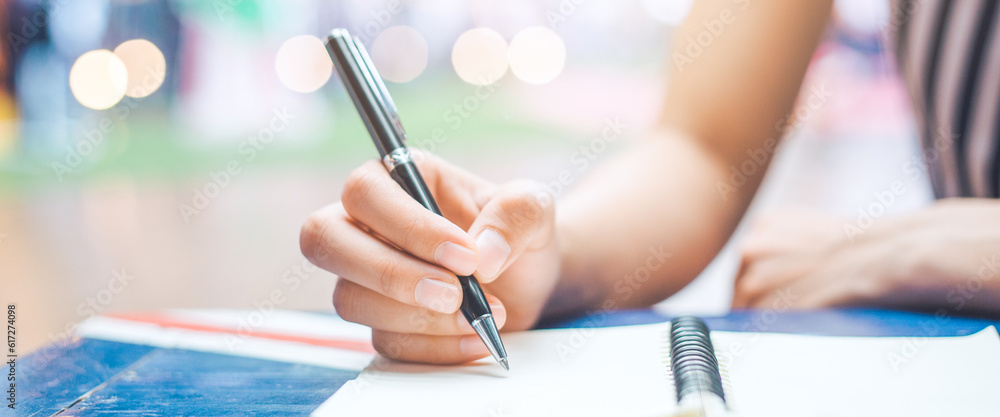 Woman hand is writing on a notepad with a pen on wooden desk.