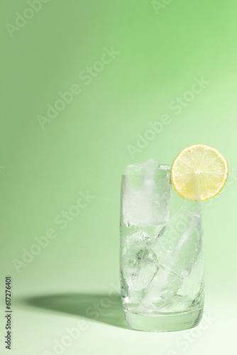 Cold glass full of ice with a lime, ready to serve light green with cast shadow.