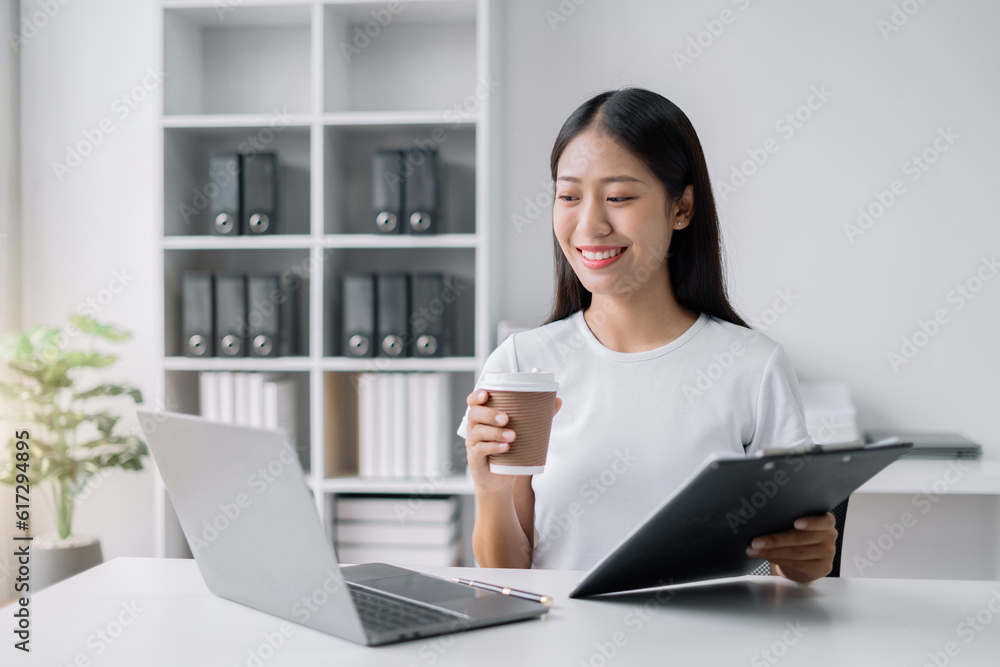 Asian businesswoman sits in a office working on laptop and enjoys a coffee. Asian businesswoman sits in a office working on laptop and enjoys a coffee.