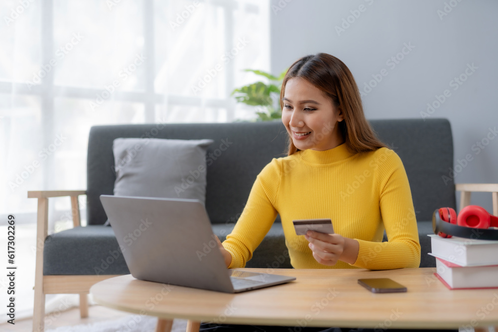 Happy young Asian woman using laptop computer and credit card for online shopping at home. Young Asian female happily utilizes her laptop and credit card for convenient online purchases. Happy young Asian woman using laptop computer and credit card for online shopping at home. Young Asian female happily utilizes her laptop and credit card for convenient online purchases.