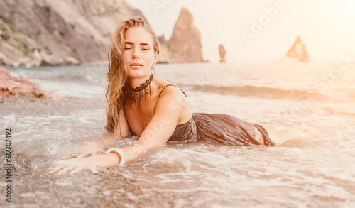 Woman summer travel sea. Happy tourist in black dress enjoy taking picture outdoors for memories. Woman traveler posing on sea beach surrounded by volcanic mountains  sharing travel adventure journey