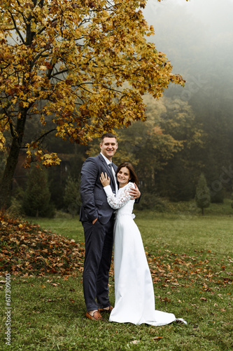 beautiful wedding couple walks in the autumn season. a tall young groom and a short bride. fallen leaves and fog. wedding in style. © Vadym