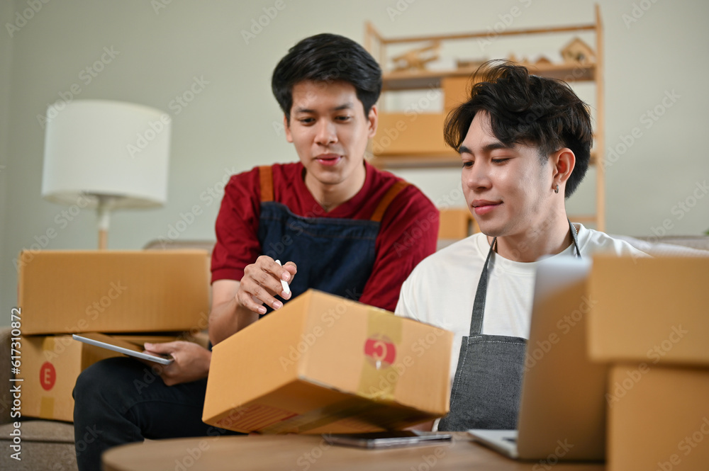 A happy Asian man checking and preparing shipping orders and working with his boyfriend A happy Asian man checking and preparing shipping orders and working with his boyfriend