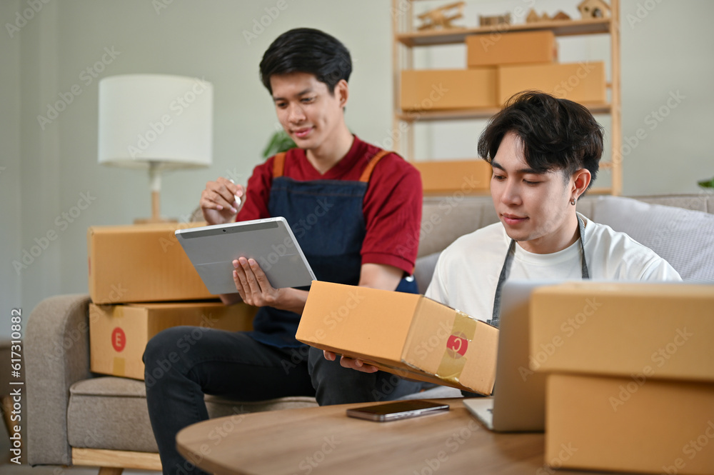 A happy Asian gay couple updating new products on the website, working at home together. A happy Asian gay couple updating new products on the website, working at home together.