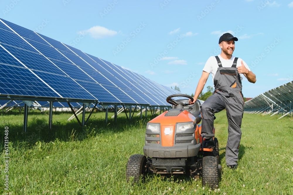 Fototapeta premium A man mows the grass near the solar panels. Green energy
