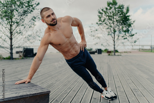 Shirtless bearded man: side plank, endurance, good shape. Active outdoor training, sportswear.