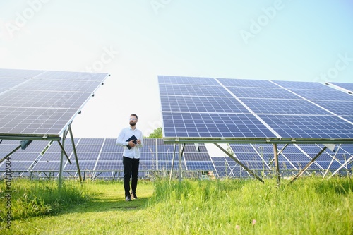 The portrait of a young engineer checks with tablet operation with sun  cleanliness on field of photovoltaic solar panels. Concept  renewable energy  technology  electricity  service  green power.