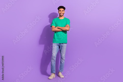 Full length body photo of young confident man wear green t-shirt denim levis brand jeans folded arms smiling isolated on purple background © deagreez
