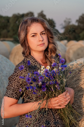 Portrait of attractive young woman in retro dress with a bouquet of wildflowers in countryside.