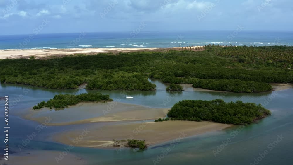 Left trucking aerial drone shot of a boat anchored in the Guaraíras Lagoon during low tide with sand banks and patches of mangroves with the Muquiço Beach in the background in Tibau do Sul, Brazil