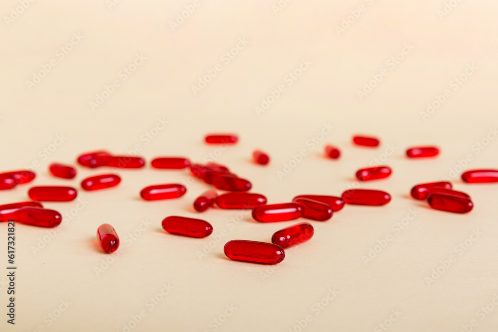 Heap of red pills on colored background. Tablets scattered on a table. Pile of red soft gelatin capsule. Vitamins and dietary supplements concept Heap of red pills on colored background. Tablets scattered on a table. Pile of red soft gelatin capsule. Vitamins and dietary supplements concept