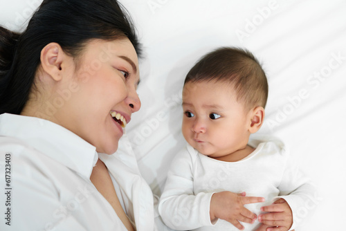 happy mother lying with her infant baby on bed (top view)