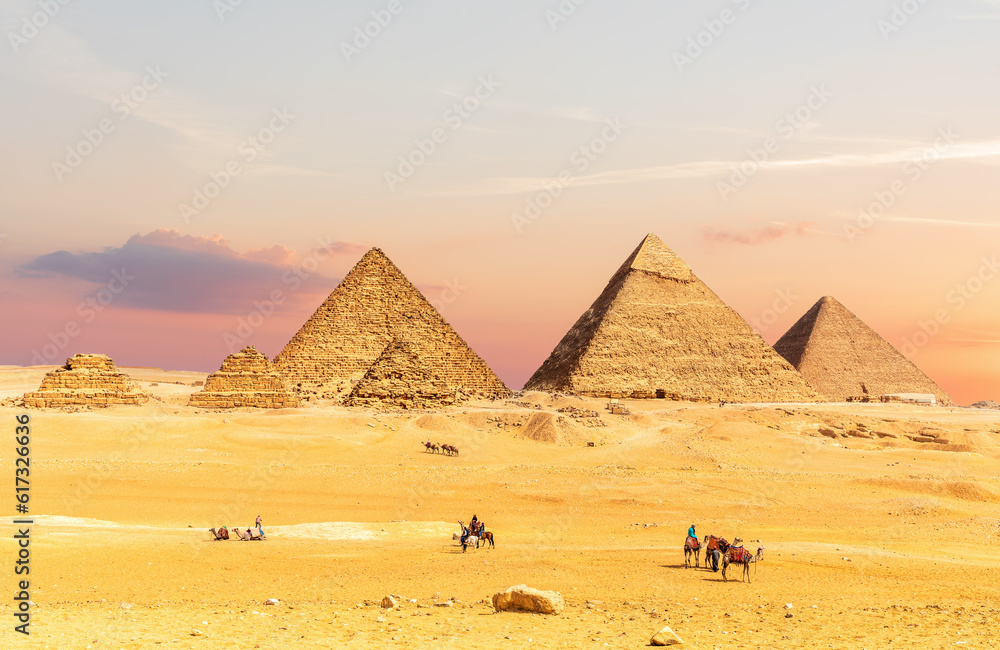 Pyramids of Egypt at sunset with tourists nearby, Giza desert, Cairo