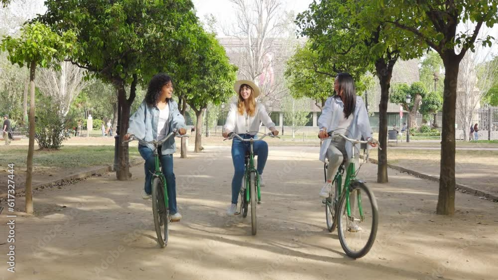 Young group of multiracial women having fun riding bike together in the park. Three smiling female friends enjoying time together on summer vacation. Friendship and holidays concept. Young group of multiracial women having fun riding bike together in the park. Three smiling female friends enjoying time together on summer vacation. Friendship and holidays concept.