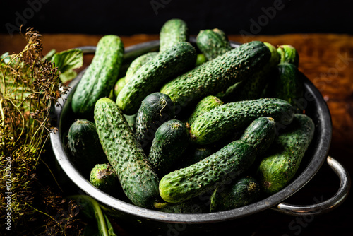 Fresh organic cucumbers in a sieve on a dark wooden background. Preparing for pickling.