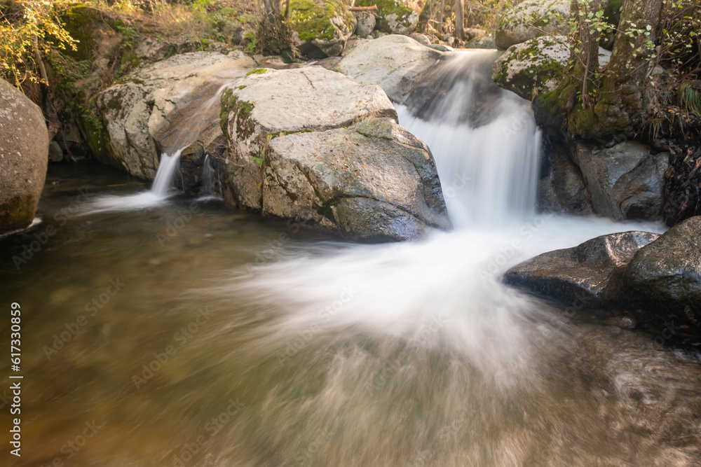 Obraz premium Small waterfall in a river whose flow runs between large granite stones deep in a dark forest. Concept of peace and relaxation, water stream and silk water.