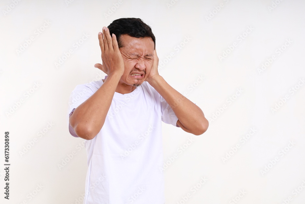 Depressed asian funny man standing while covering his ears. Isolated on white background Depressed asian funny man standing while covering his ears. Isolated on white background
