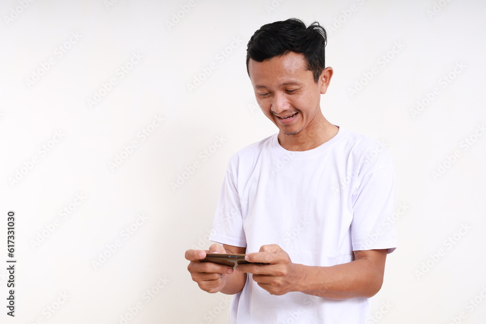 Happy Asian funny man standing while playing game with his smart phone. Isolated on white Happy Asian funny man standing while playing game with his smart phone. Isolated on white