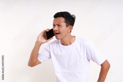 Shocked angry asian funny man standing while on the phone. Isolated on white background