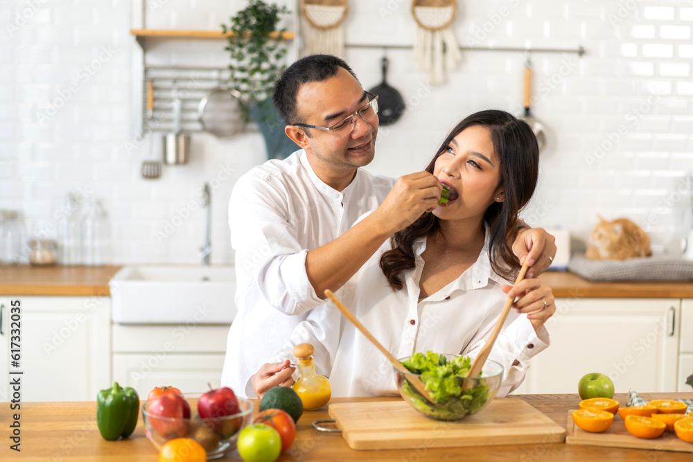 Young asian family couple having fun cooking and preparing cook vegan food healthy eat with fresh vegetable salad on counter in kitchen at home.Happy couple looking to preparing food Young asian family couple having fun cooking and preparing cook vegan food healthy eat with fresh vegetable salad on counter in kitchen at home.Happy couple looking to preparing food