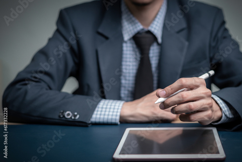 Businessman writes signing contract, designs, draws, or sketches projects through a tablet on the office desk. Hand concept stamp of approval on a public notarization certificate document electronic.